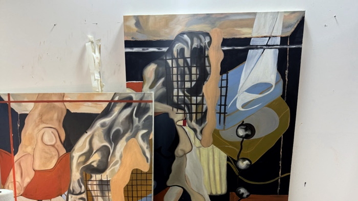 a small artist studio with paintings against the wall and a small desk and trolley with art supplies.