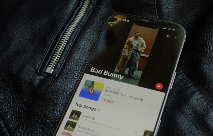a phone laid on top of a black leather jacket with a zip to the left of the image. The phone screen shows Bad Bunny’s Top Songs.