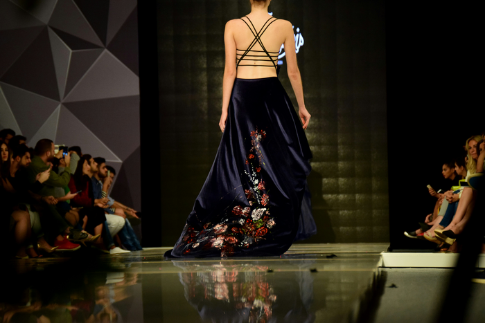 a woman in a navy spaghetti strap dress walks away on the catwalk.