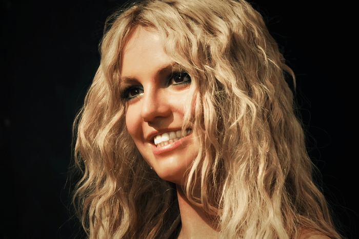 A close up image of Britney Spears smiling with a black background.